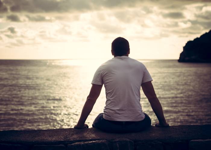 A guy sits by the sea and looks at the sunset