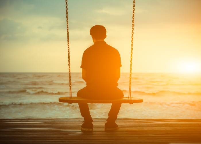 A guy sits on a swing by the sea